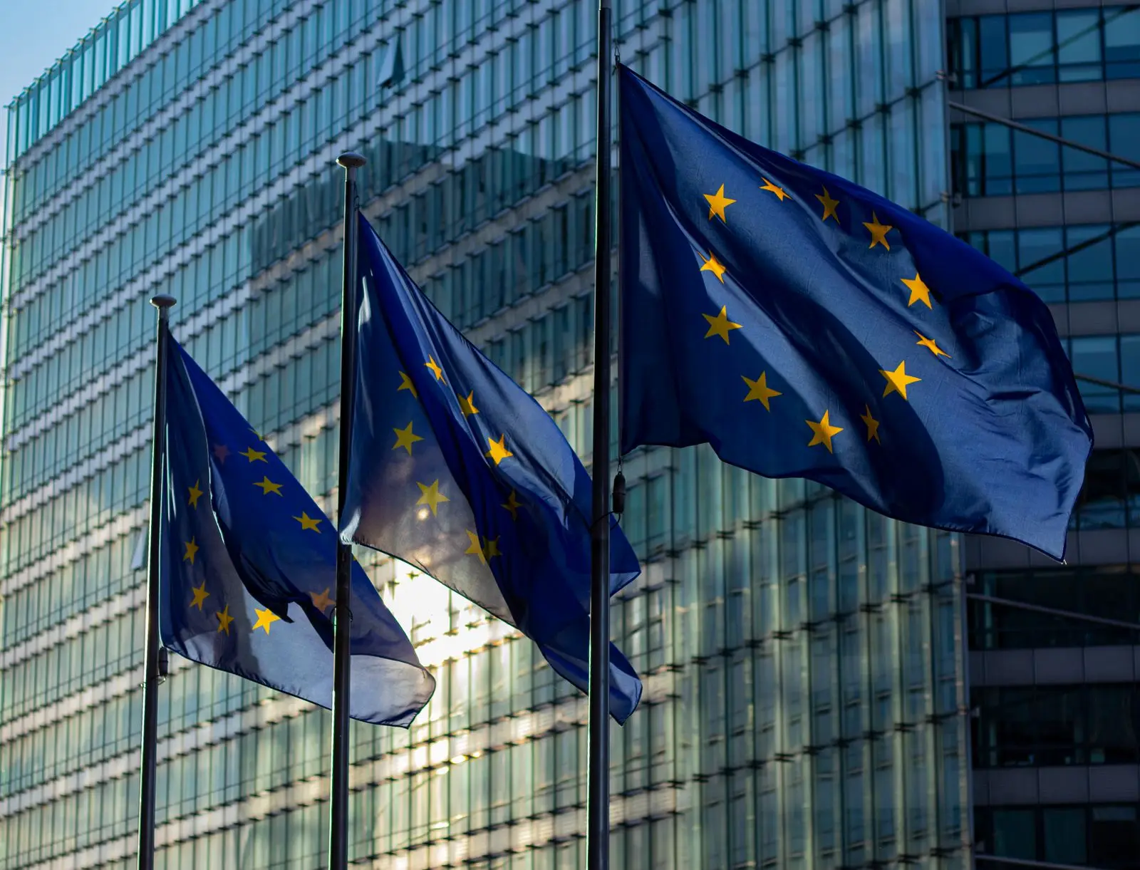 Drie Europese vlaggen wapperen voor de glazen gevel van een kantoorgebouw in Brussel