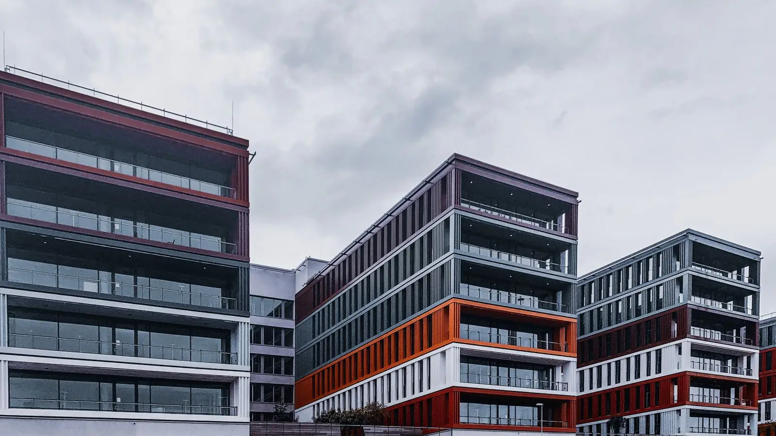 Moderne kantoorgebouwen met glazen gevels en rode en oranje banden onder een grijze lucht, in het havengebied van Frankfurt