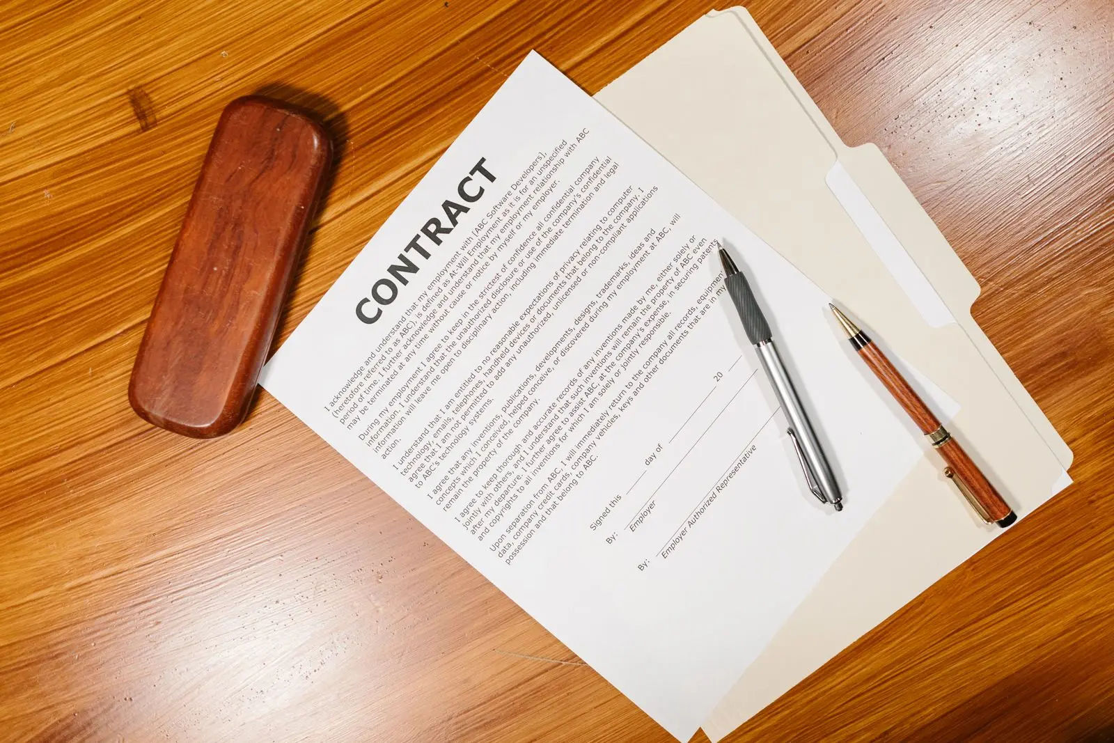 Een contract op een houten bureau, met een map en twee pennen ernaast