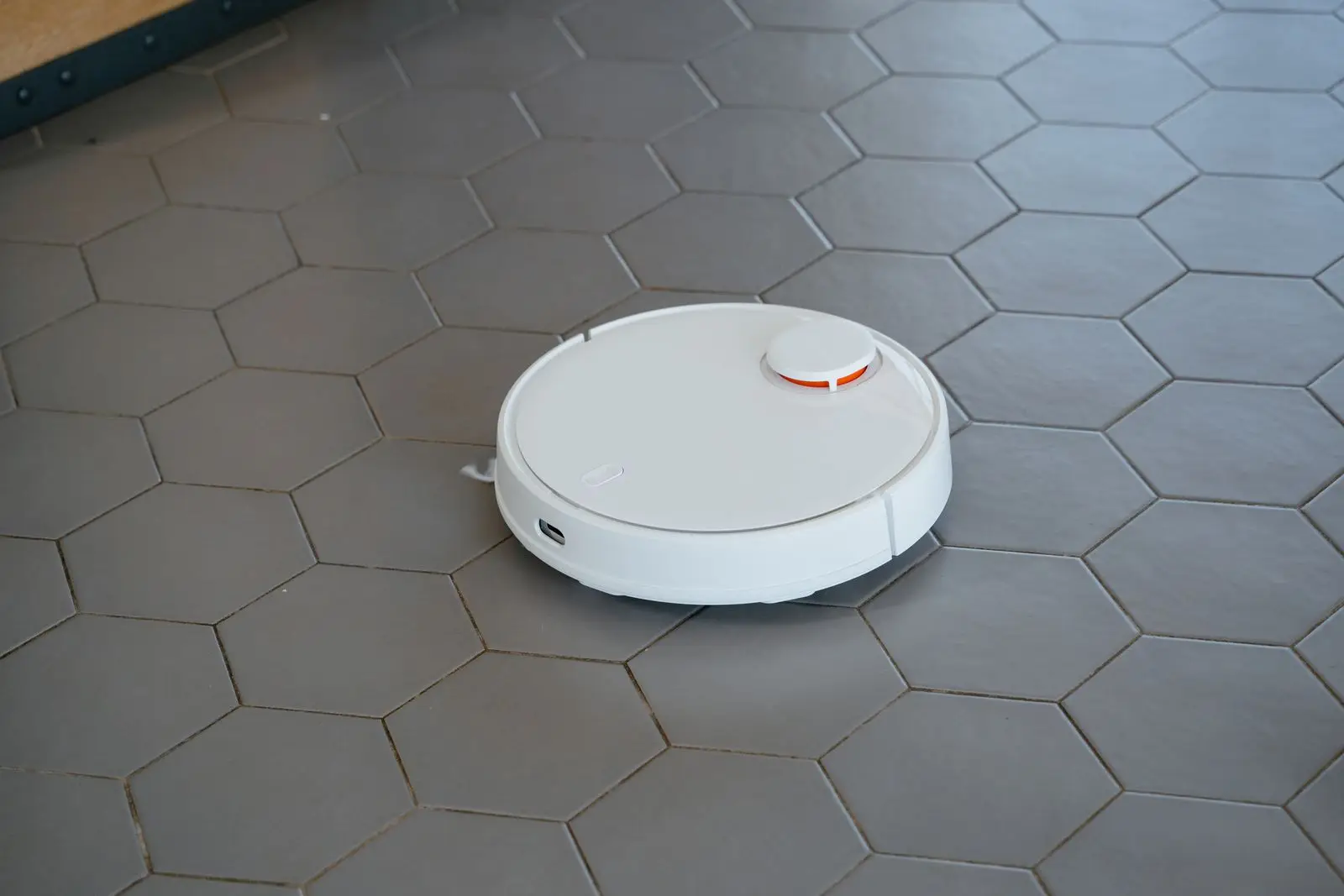 Een witte robotstofzuiger rijdt over een vloer van grijze zeshoekige tegels.