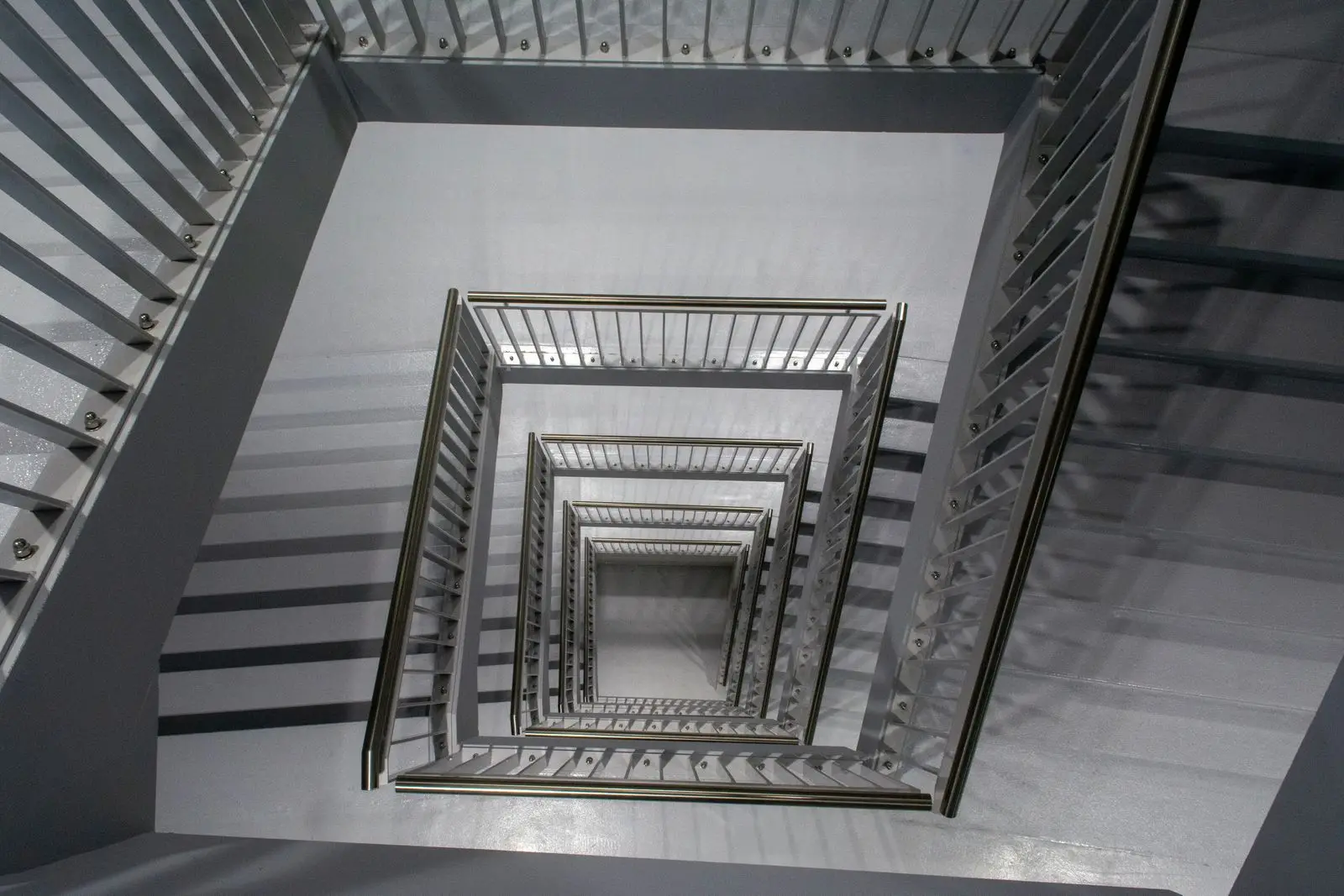 Blik omlaag in een wit trappenhuis in Leiden, met vierkant om elkaar heen lopende trappen en metalen leuningen.