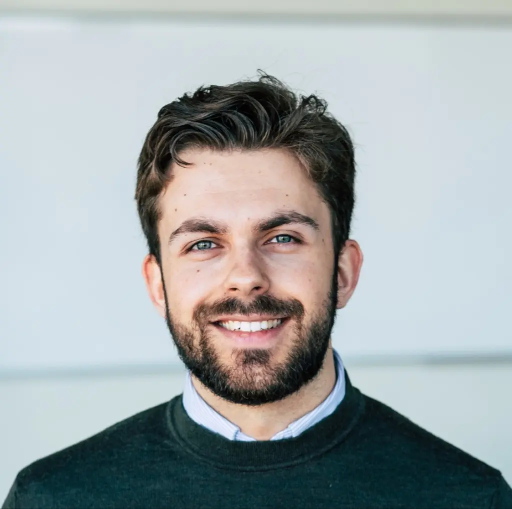 Portret van Steijn de Ridder van Facility Finder, lachend in een donkergroene trui voor een lichte wand
