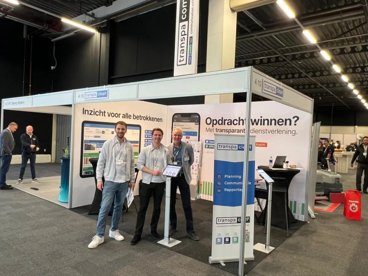 Drie mensen van TranspaClean in hun stand op een vakbeurs, met banners over planning, communicatie en rapportage